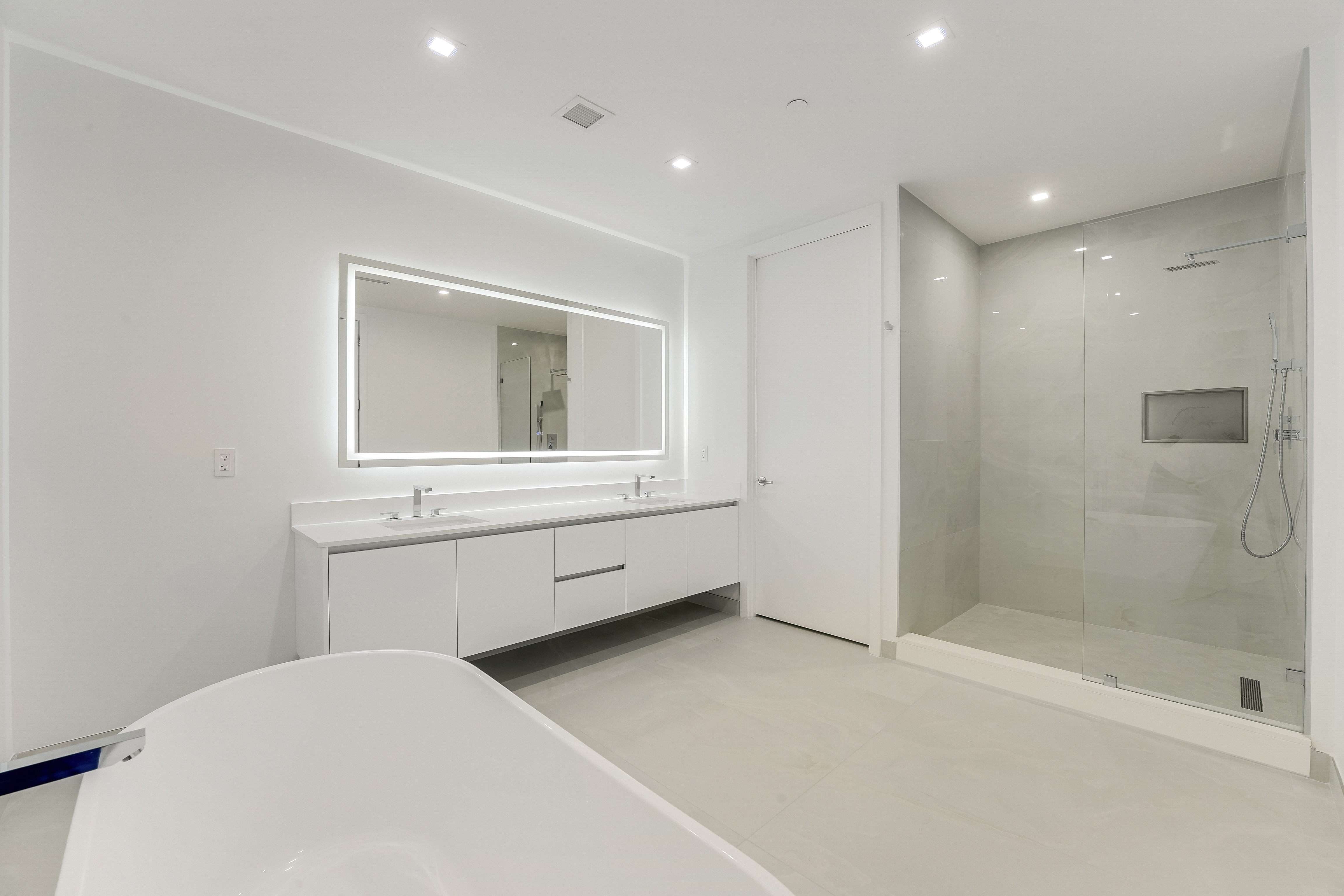 Primary bathroom with freestanding tub, illuminated mirror and glass shower in Executive 704